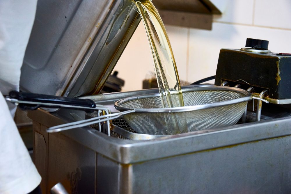 Kitchen worker pours grease through metal sieve into grease trap