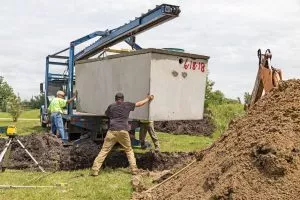 Workers place a septic tank into the ground after excavating a mound of soil