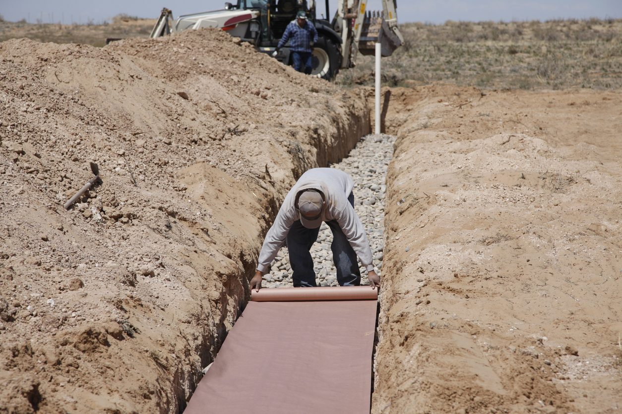 Technician lays a barrier layer in a trenching system for a septic system