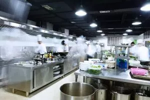 Busy restaurant kitchen with stainless steel stations and multiple staff prepares for dinner rush